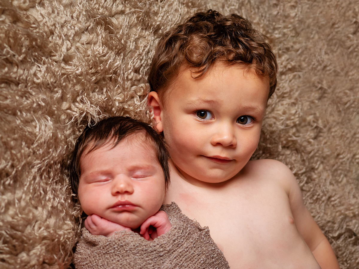 A newborn and older sibling together in a studio portrait