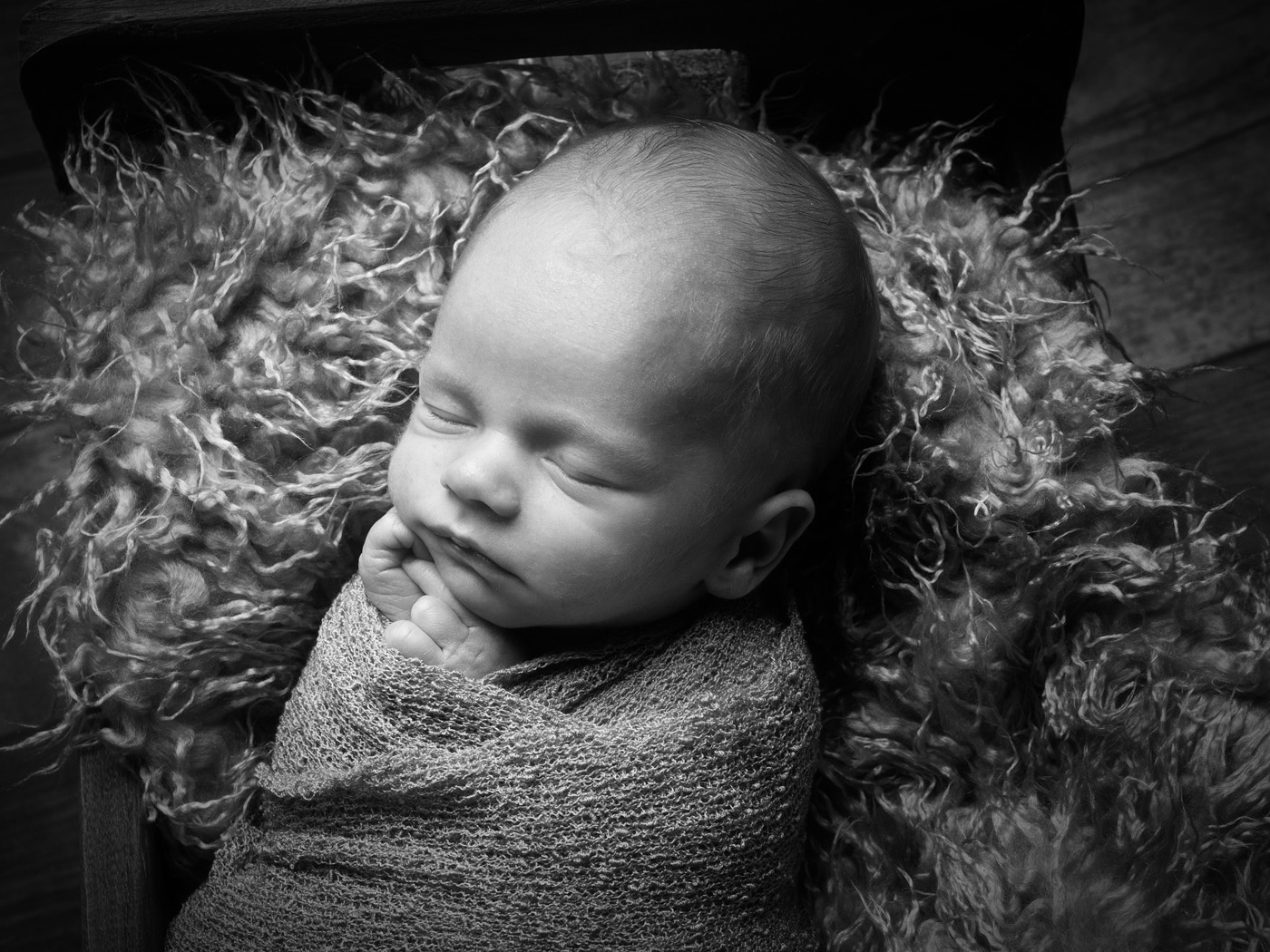 A sleeping newborn wrapped in a textured blanket, photographed in black and white by Infinity Photographic Studios